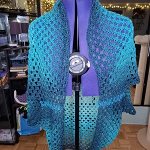 May include: A teal and blue crocheted shawl with a lacy pattern. The shawl is draped over a dress form.