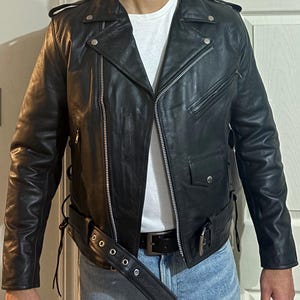 May include: A black leather motorcycle jacket with a zipper closure and a belt. The jacket has a zippered pocket on the left side and a snap closure on the collar.