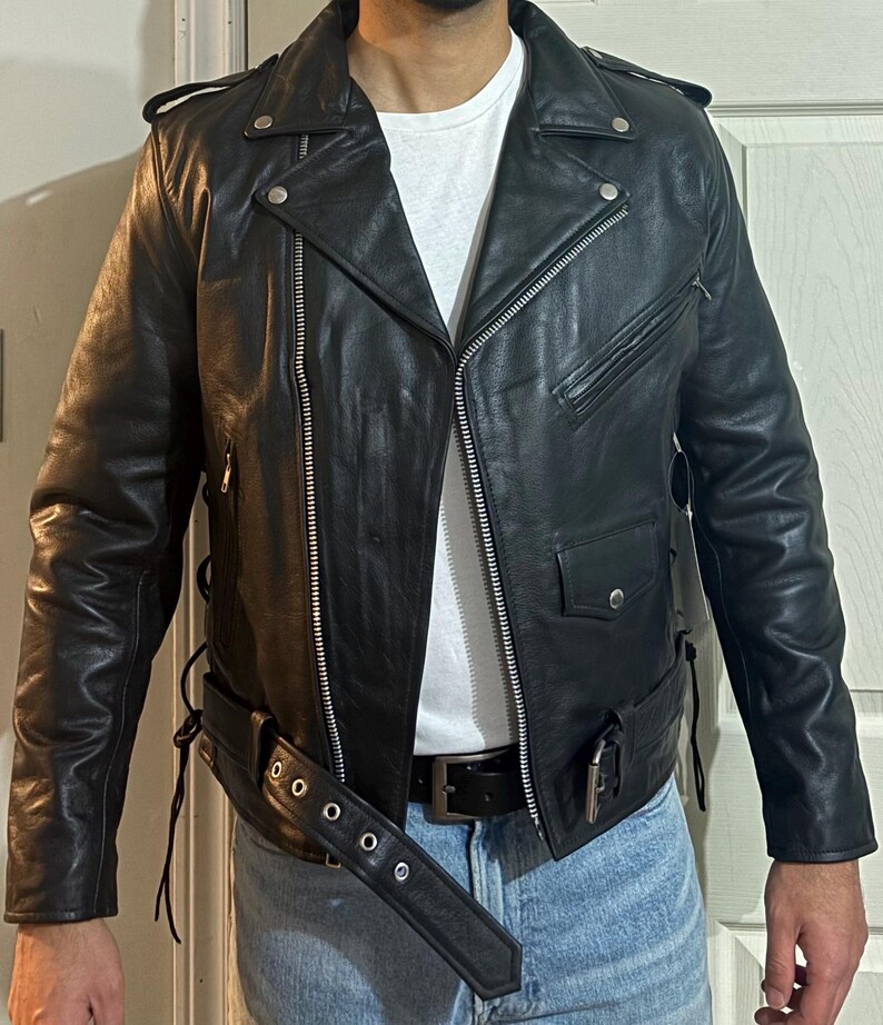 May include: A black leather motorcycle jacket with a zipper closure and a belt. The jacket has a zippered pocket on the left side and a snap closure on the collar.