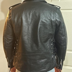 May include: Black leather jacket with a zipper closure and lace-up detailing on the sides. The jacket has a classic biker style.