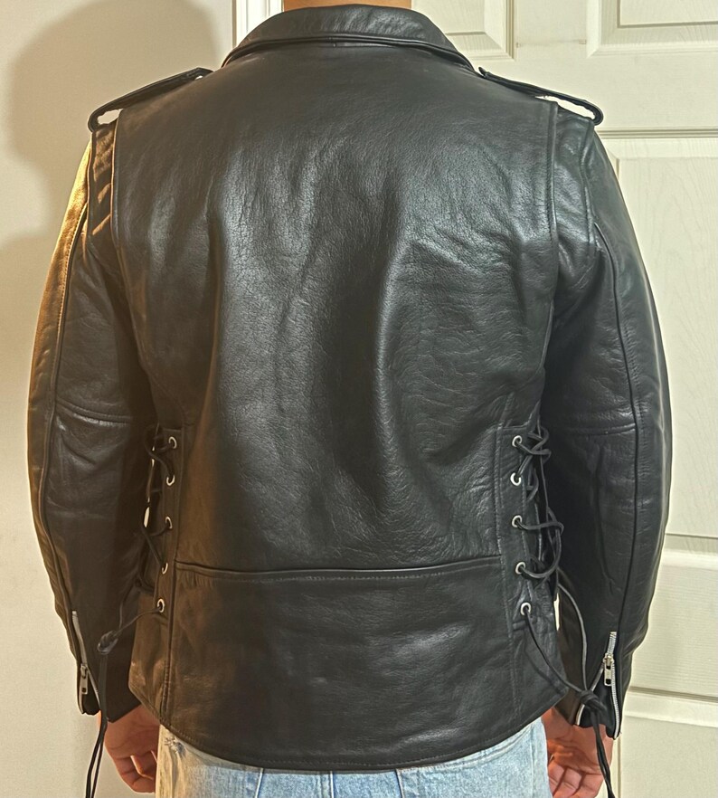 May include: Black leather jacket with a zipper closure and lace-up detailing on the sides. The jacket has a classic biker style.