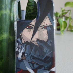 Op de afbeelding: Transparante telefoonhoes met een anime-stijl illustratie. Het ontwerp toont een personage met donker haar en intense rode ogen. Het kunstwerk gebruikt zwart, grijs en rood, wat een opvallend beeld cre&euml;ert.