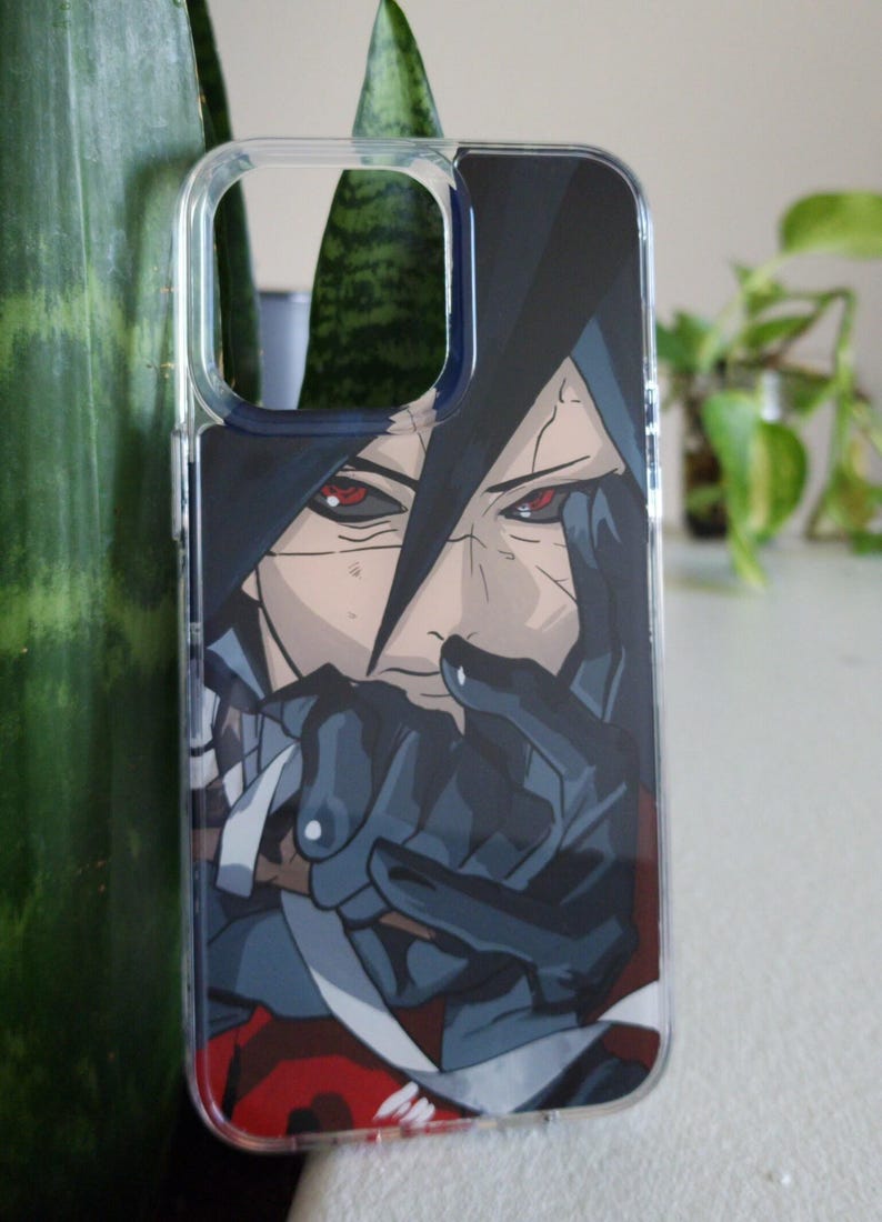 Op de afbeelding: Transparante telefoonhoes met een anime-stijl illustratie. Het ontwerp toont een personage met donker haar en intense rode ogen. Het kunstwerk gebruikt zwart, grijs en rood, wat een opvallend beeld cre&euml;ert.