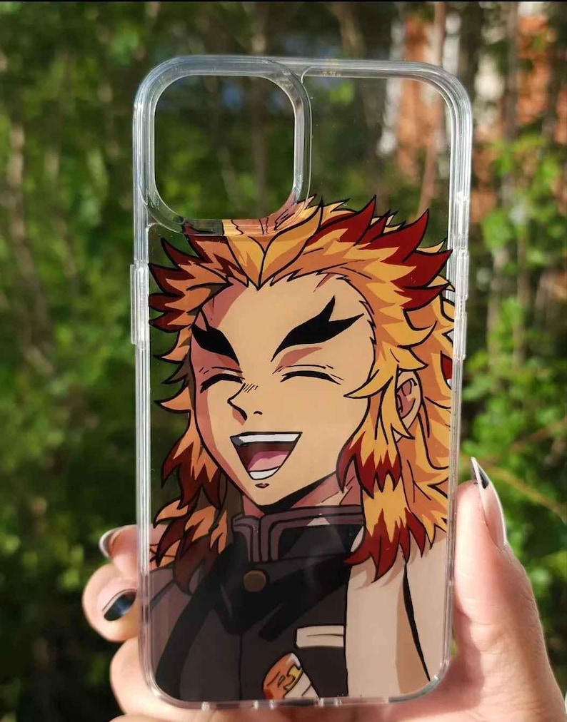 Op de afbeelding: Transparante telefoonhoes met een lachend anime-personage met geel en rood haar. Het personage draagt een zwart uniform met een witte kraag. De hoes wordt tegen een vage groene achtergrond gehouden.
