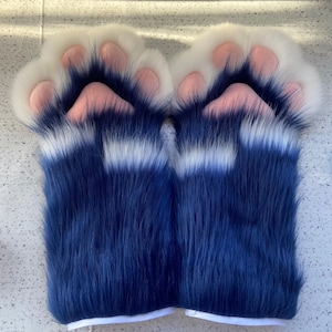 Puede incluir: Un par de títeres de mano de felpa azul y blanco con almohadillas de patas rosas.