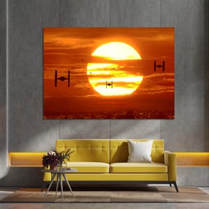 May include: A digital art print featuring a sunset with a large orange sun and four black TIE fighters flying in formation. The print is framed and hanging on a wall in a modern living room.
