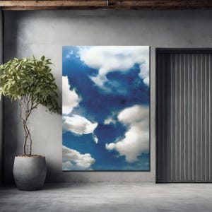 May include: A large rectangular canvas print depicting a vibrant blue sky filled with fluffy white clouds. The artwork is displayed on a gray wall, next to a tall, potted plant and a gray metal door.