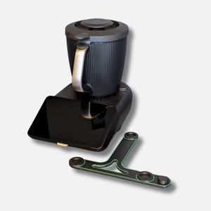 Può includere: Una macchina da caffè nera con manico e coperchio argentati. La macchina da caffè poggia su una base nera con un vassoio rettangolare. Un accessorio nero e verde è in primo piano.
