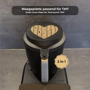 Könnte beinhalten: Schwarzes und silbernes Küchengerät mit herzförmigem Holzdesign auf der Oberseite. Der Text oben lautet "Scale Cover Plate for Thermomix TM7". Ein kleiner Aufkleber auf der Vorderseite lautet "2 in 1".