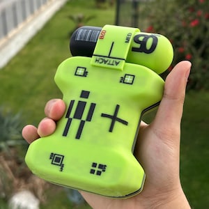 Könnte beinhalten: Ein limettengrünes medizinisches Gerät mit schwarzen Akzenten wird in einer Hand gehalten. Das Gerät hat eine pillenförmige Komponente mit der Nummer "05" und dem Wort "MED" aufgedruckt. Auf dem Gerät steht auch das Wort "ATTACH".