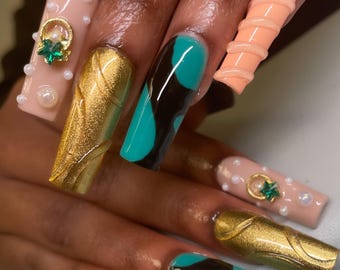 May include: Long, colourful, and decorated acrylic nails. The nails are painted in shades of teal, black, gold, and peach. Some nails have a swirl design, while others have a 3D design. The nails are decorated with small pearls and rhinestones.