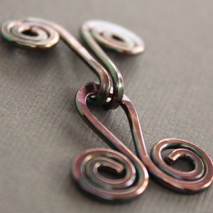 May include: A metallic, iridescent, double-looped, wire pendant with a swirl design. The pendant is made of copper wire and has a rainbow-like finish.