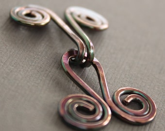 May include: A metallic, iridescent, double-looped, wire pendant with a swirl design. The pendant is made of copper wire and has a rainbow-like finish.