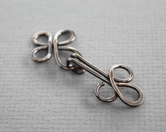 May include: A silver-toned metal hook and eye closure with a decorative design. The hook is shaped like a clover and the eye is shaped like a figure of eight.