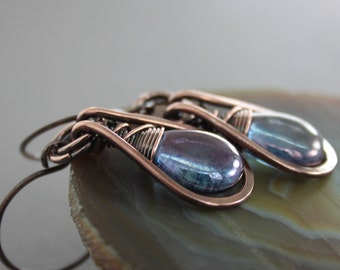 May include: A pair of copper wire wrapped earrings with iridescent blue teardrop shaped glass beads.