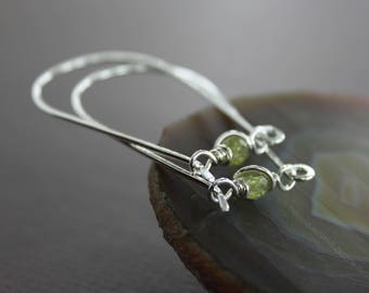 May include: Silver hoop earrings with green gemstone accents. The earrings are made of thin wire and have a simple, elegant design.