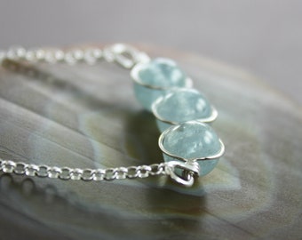 May include: A silver chain necklace with three light blue aquamarine beads. The beads are round and have a smooth, polished finish.