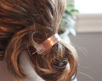May include: A copper hair clip with a smooth, polished finish. The clip is designed to hold hair in place and is a simple, elegant accessory.