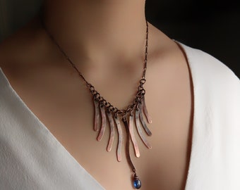 May include: A copper necklace featuring a cascading design of hammered copper strips and a single blue gemstone pendant.