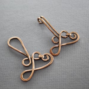 May include: Two copper wire heart-shaped charms with a loop at the top for attaching to jewelry or other crafts.