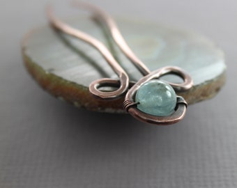 May include: A copper hair pin with a light blue gemstone. The pin is twisted into a decorative shape.