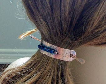 May include: A silver hair stick with a hammered finish and a row of blue beads. The stick is bent into a loop and has a thin metal pin that goes through the loop.