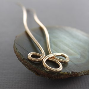 May include: A gold-toned hair pin with a decorative loop design. The pin is resting on a green and brown agate stone.
