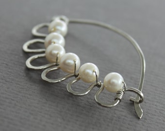 May include: A silver nose ring with a curved wire and a row of white pearls attached to the wire.