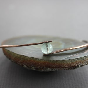 May include: A delicate copper bangle bracelet with a single light blue gemstone bead.