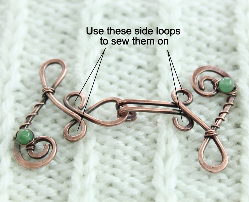 May include: Copper wire toggle clasp with two green gemstone accents. The clasp has two side loops for sewing onto fabric. "Use these side loops to sew them on" is written above the clasp.