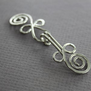 May include: Silver wire hair clip with a double swirl design.