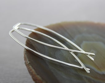 May include: A pair of silver hoop earrings with a simple, minimalist design. The earrings are made of thin, smooth wire and are slightly curved.