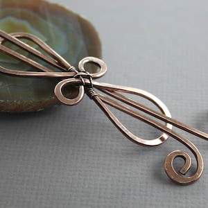 May include: A copper wire hair clip with a decorative design featuring a swirl and a teardrop shape.