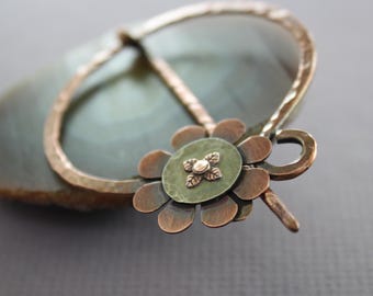 May include: A copper brooch featuring a green agate stone and a copper flower design. The flower has a small copper centre with a gold dot.