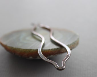 May include: A silver wavy hair clip, made of metal, is resting on a white and brown shell.