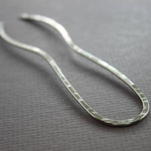 May include: A silver hair stick with a hammered finish and a curved shape.