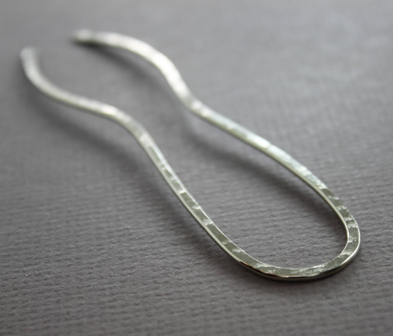 May include: A silver hair stick with a hammered finish and a curved shape.