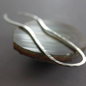 May include: A silver hammered metal earring with a curved, oval shape.