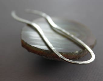 May include: A silver hammered metal earring with a curved, oval shape.
