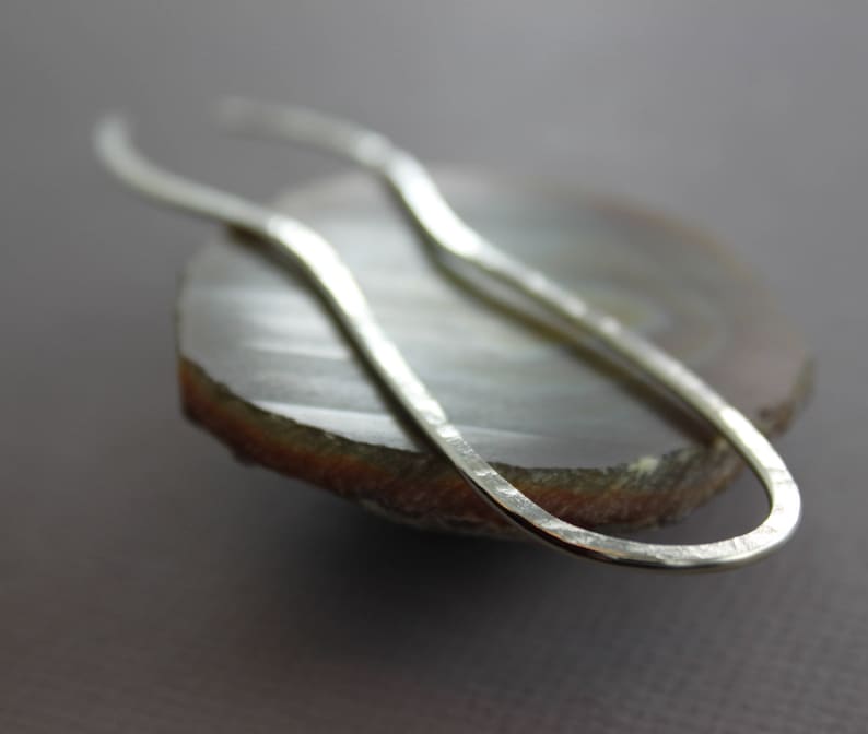 May include: A silver hammered metal earring with a curved, oval shape.