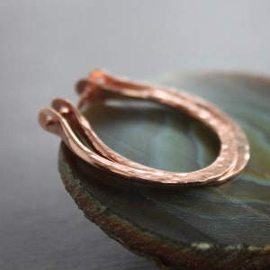 May include: A pair of hammered copper hoop earrings. The earrings are a simple, minimalist design and are made of a thick gauge of copper wire.