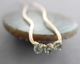 May include: A gold hair stick with three light green faceted glass beads. The hair stick is curved and has a simple design.