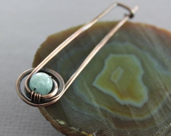 May include: A copper wire brooch with a light blue gemstone in the centre. The brooch is on a slice of agate.