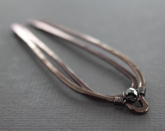 May include: A double-pronged hair clip made of copper wire with a dark grey gemstone accent.