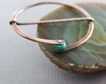 May include: A copper wire ring with a turquoise stone accent. The ring is on a brown and green agate slice.