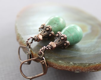 May include: A pair of copper dangle earrings with green gemstone drops. The earrings have a detailed, ornate design and feature a hook fastening.