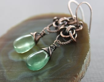 May include: A pair of copper wire wrapped earrings featuring green teardrop shaped stones. The earrings have a delicate, intricate design and are perfect for adding a touch of bohemian style to any outfit.