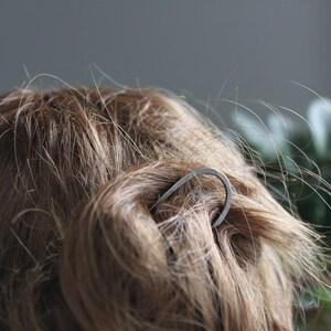 May include: A silver hair clip in the shape of a curved line, holding back a woman's brown hair.