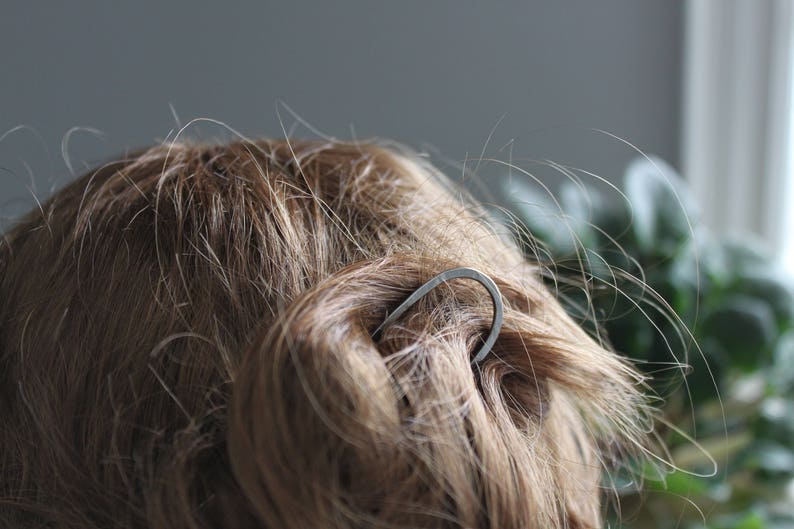 May include: A silver hair clip in the shape of a curved line, holding back a woman's brown hair.