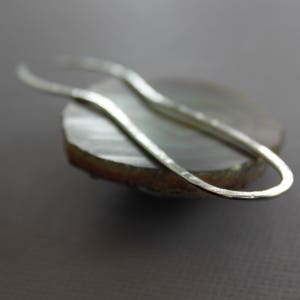 May include: A silver, hammered, open-ended loop earring. The earring is resting on a piece of agate.